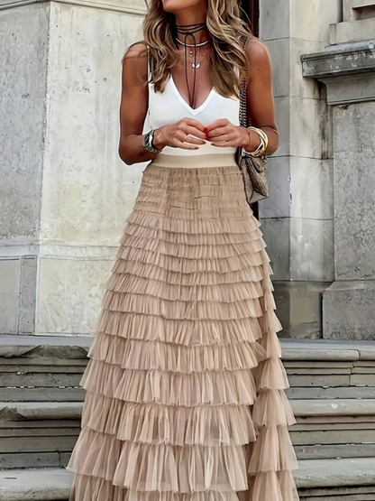 Woman wearing the Sophie Women's Layered Tulle Skirt, a ruffled skirt with multiple soft layers, creating a flowing and voluminous look, styled with a sleeveless top and accessories, standing on steps outdoors.