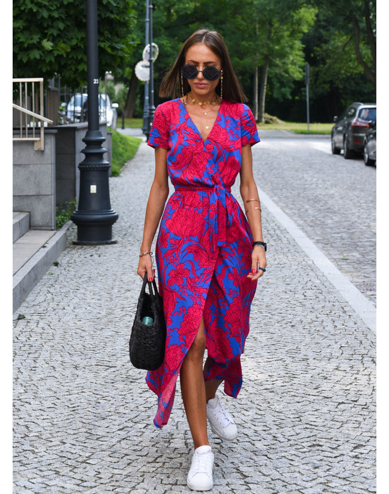 A woman walking down a street wearing the Lana Women's Elegant Wrap Dress, a casual midi dress with a flattering wrap design and tie waist, styled with sneakers and a woven handbag. This versatile dress is ideal for both casual outings and stylish gatherings.