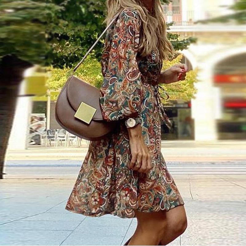 Model wearing the Esme Women's Boho Mini Dress with flowing sleeves and intricate paisley patterns, perfect for a chic, bohemian look. The dress offers a relaxed fit, ideal for casual outings or warm-weather events, styled with a crossbody bag and delicate accessories.