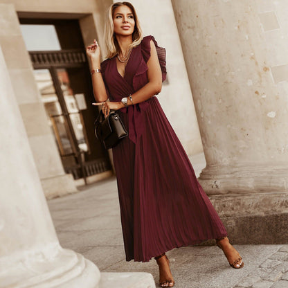 Woman wearing the Amara | Ruffled Sleeveless Pleated Maxi Dress, featuring elegant ruffles and a flowing pleated design, styled with heels and a handbag in an urban outdoor setting.