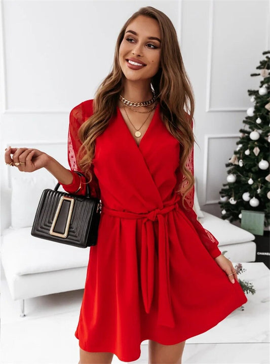 Woman wearing the Elena Women's Mesh Sleeve Wrap Dress, a mini dress with a flattering wrap design and stylish mesh sleeves, accessorized with layered necklaces and bracelets, posing elegantly in a chic indoor setting.