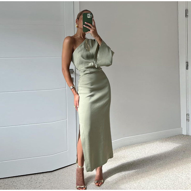 Woman wearing the Amelia Women's One-Shoulder Midi Dress, showcasing an elegant, sleek design with a side slit, standing in a modern interior setting. Perfect for formal occasions or sophisticated outings.