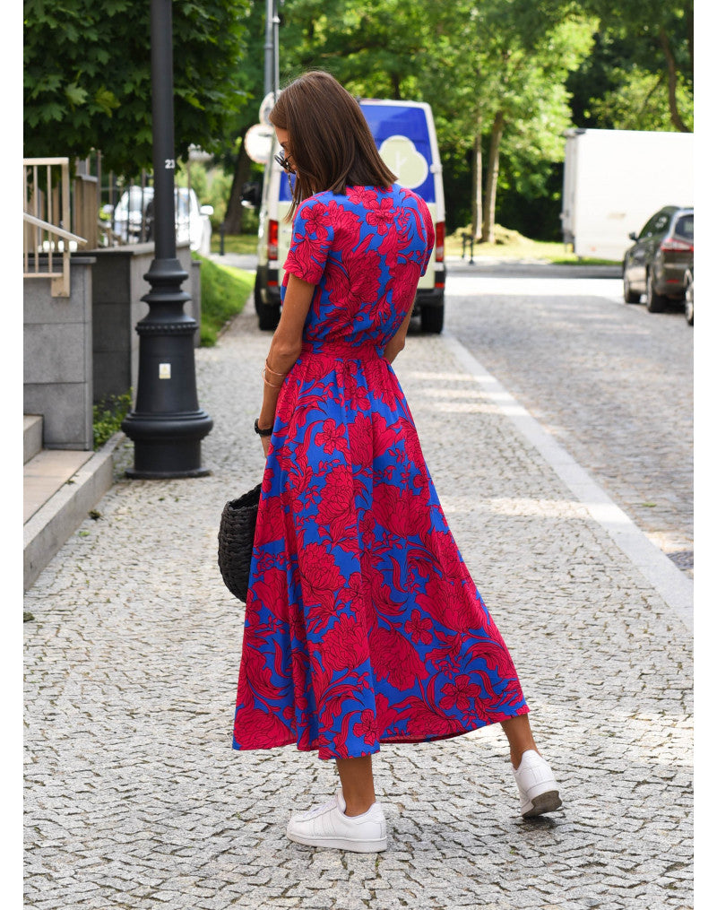 A woman walking down a street wearing the Lana Women's Elegant Wrap Dress, a casual midi dress with a flattering wrap design and tie waist, styled with sneakers and a woven handbag. This versatile dress is ideal for both casual outings and stylish gatherings.