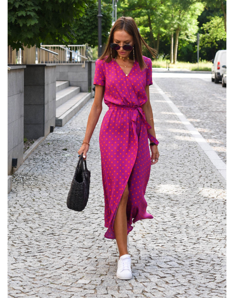 A woman walking down a street wearing the Lana Women's Elegant Wrap Dress, a casual midi dress with a flattering wrap design and tie waist, styled with sneakers and a woven handbag. This versatile dress is ideal for both casual outings and stylish gatherings.