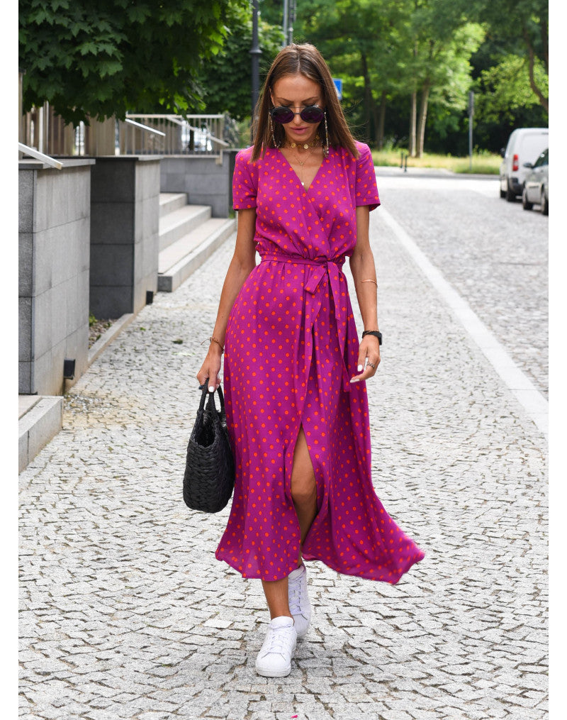 A woman walking down a street wearing the Lana Women's Elegant Wrap Dress, a casual midi dress with a flattering wrap design and tie waist, styled with sneakers and a woven handbag. This versatile dress is ideal for both casual outings and stylish gatherings.