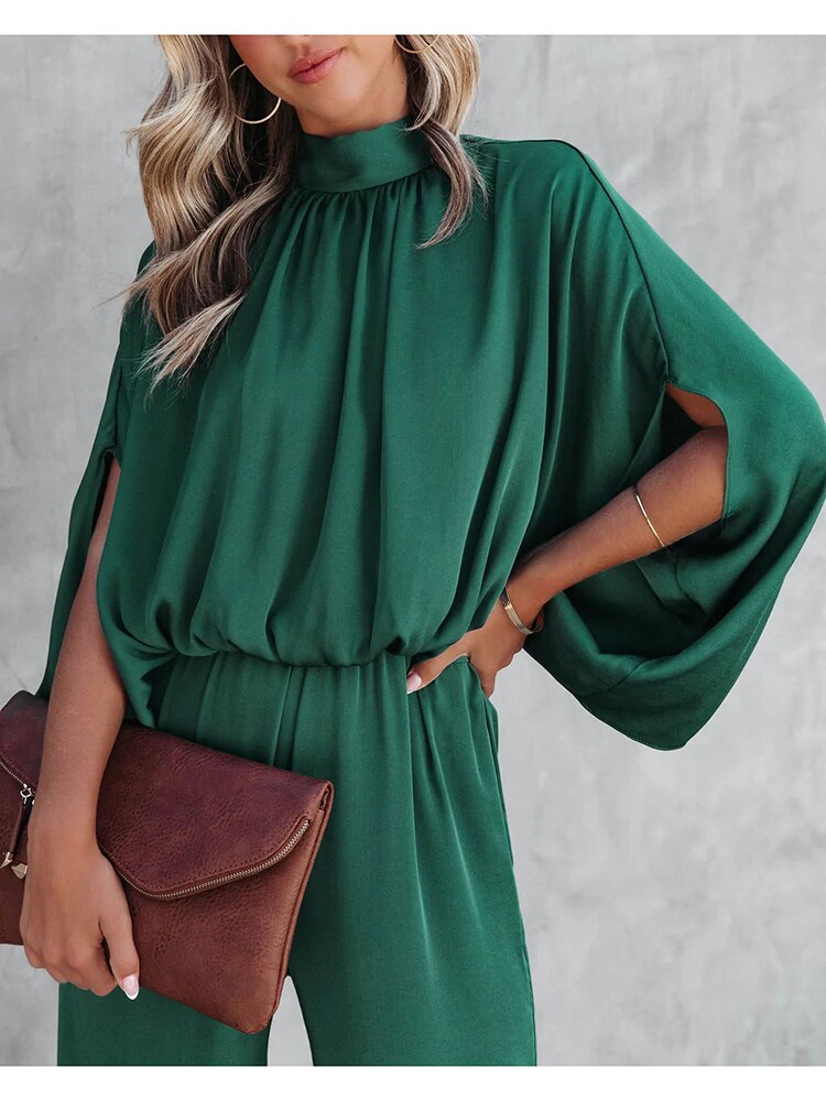 A woman wearing a high-neck, wide-leg dress with flowing sleeves, styled elegantly with a clutch bag. The dress features a relaxed silhouette that combines sophistication with comfort, perfect for both casual and formal occasions.