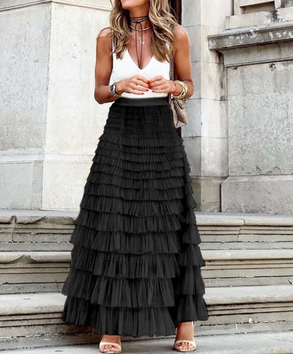 Woman wearing the Sophie Women's Layered Tulle Skirt, a ruffled skirt with multiple soft layers, creating a flowing and voluminous look, styled with a sleeveless top and accessories, standing on steps outdoors.