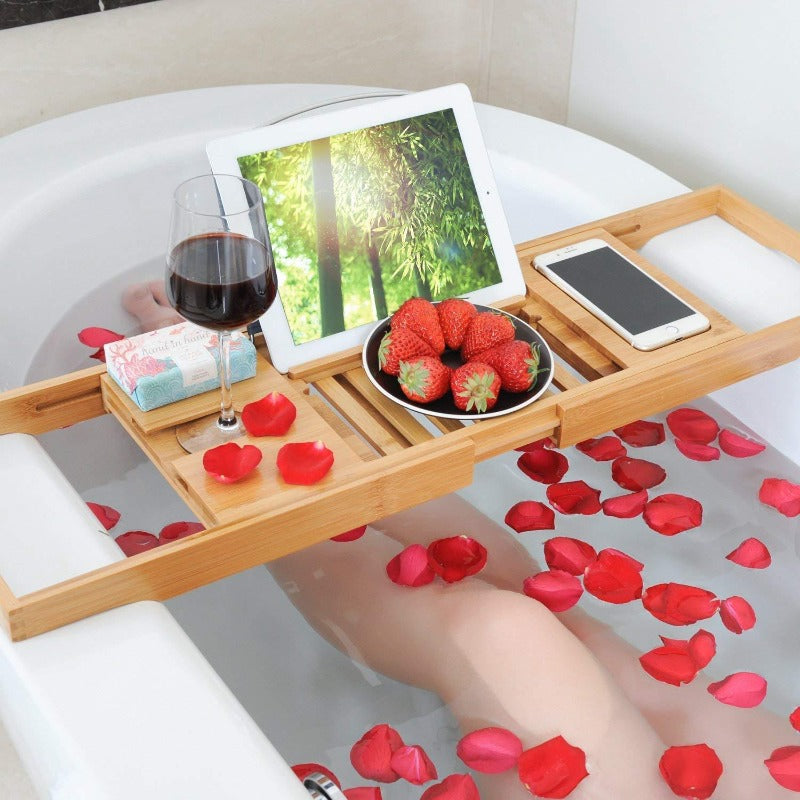 Bath tray with a multi-functional design holding a glass of wine, tablet, and smartphone on a bathtub, showcasing its compartments and adjustable layout for added convenience and relaxation.