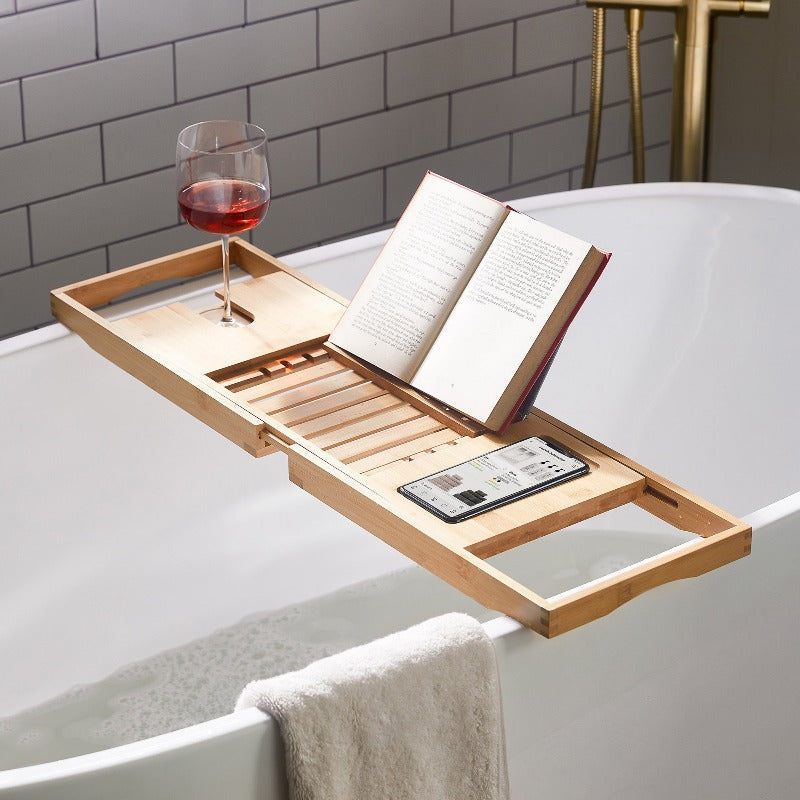 Bath tray with a multi-functional design holding a glass of wine, tablet, and smartphone on a bathtub, showcasing its compartments and adjustable layout for added convenience and relaxation.