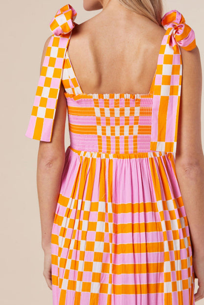 A woman wearing a stylish checkered maxi dress with a flowing skirt and bow-tie shoulder straps, creating a bold and eye-catching look. The dress exudes a statement style, perfect for casual outings or special occasions.