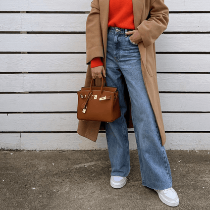 Image showing a woman holding an elegant handbag with a sleek design, featuring gold hardware and a structured shape, paired with casual attire for a stylish, sophisticated look.