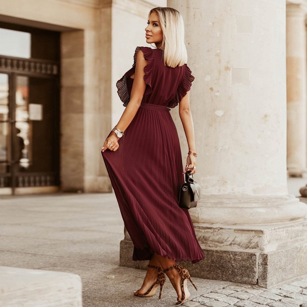 Woman wearing the Amara | Ruffled Sleeveless Pleated Maxi Dress, featuring elegant ruffles and a flowing pleated design, styled with heels and a handbag in an urban outdoor setting.