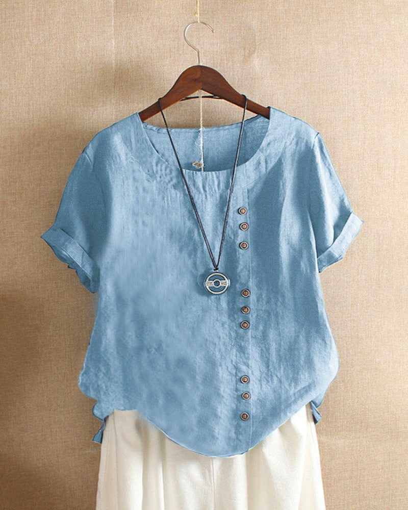 A casual women's blouse with an asymmetrical button design, short sleeves, and a relaxed fit, hanging on a wooden hanger. This blouse, part of the Mira collection, offers a unique style perfect for casual and everyday wear.