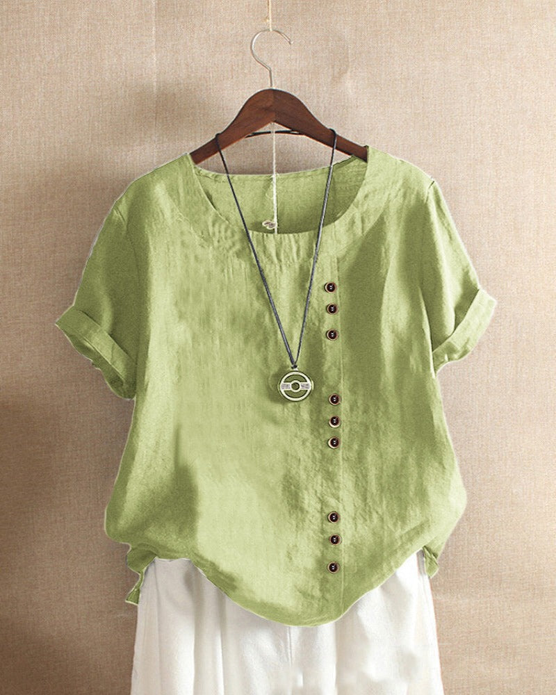 A casual women's blouse with an asymmetrical button design, short sleeves, and a relaxed fit, hanging on a wooden hanger. This blouse, part of the Mira collection, offers a unique style perfect for casual and everyday wear.