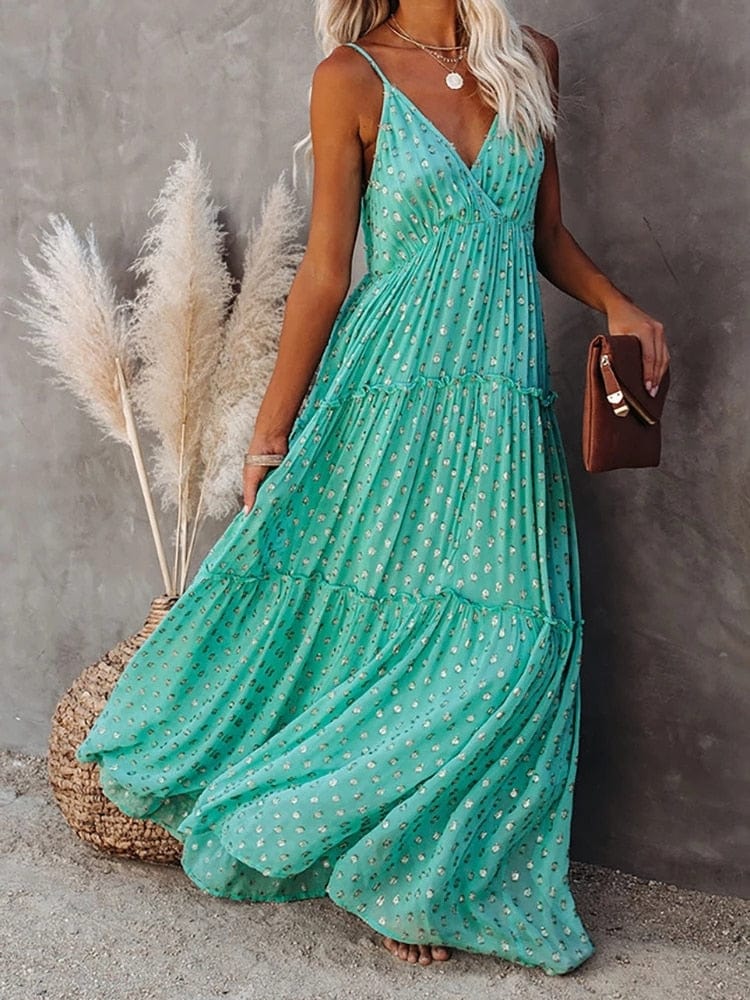 Woman wearing the Sienna Women's Tiered Maxi Dress, a long, flowy dress with adjustable straps and a bohemian-inspired tiered design, accessorized with layered necklaces and a clutch, posing gracefully against a textured wall with pampas grass in the background.