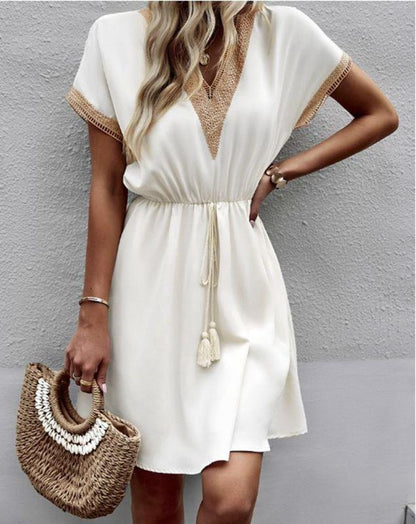 Woman wearing the Leah | Boho V-Neck Drawstring Dress with a relaxed fit and delicate detailing around the neckline. The dress is styled with a cinched waist, achieved through a drawstring, and paired with layered necklaces and a stylish handbag for a chic bohemian look.