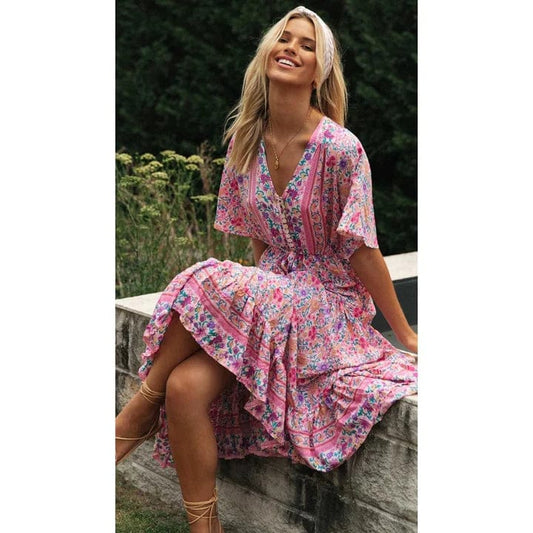 A woman sitting outdoors wearing a flowing midi dress with boho-inspired ruffles, featuring a flattering and relaxed design ideal for casual or special occasions.