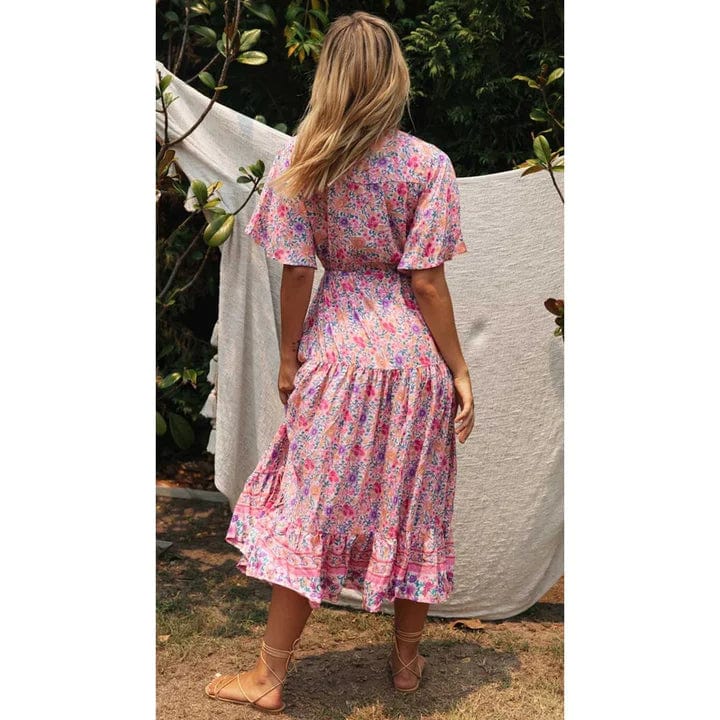 A woman sitting outdoors wearing a flowing midi dress with boho-inspired ruffles, featuring a flattering and relaxed design ideal for casual or special occasions.