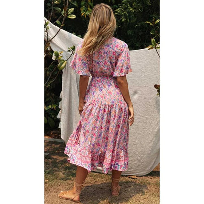 A woman sitting outdoors wearing a flowing midi dress with boho-inspired ruffles, featuring a flattering and relaxed design ideal for casual or special occasions.