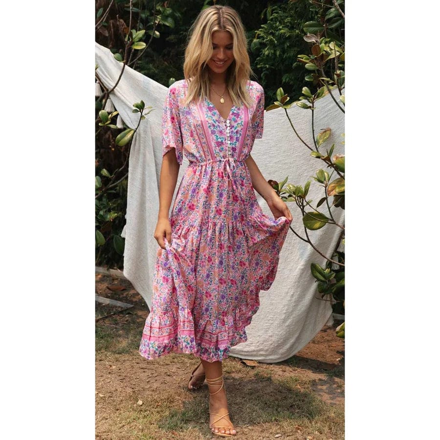 A woman sitting outdoors wearing a flowing midi dress with boho-inspired ruffles, featuring a flattering and relaxed design ideal for casual or special occasions.