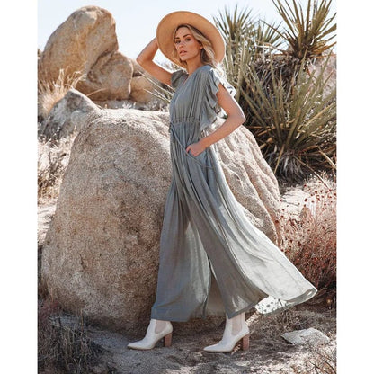 A woman wearing the Amara Women's Flowing Maxi Dress, styled with a wide-brimmed hat and ankle boots, standing outdoors among desert rocks. The dress has a boho-chic design with a relaxed, flowing silhouette, perfect for a free-spirited, elegant look.