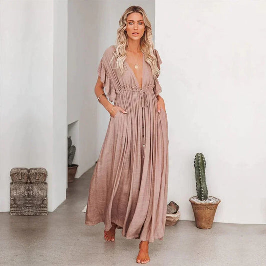 Woman wearing the Elena Women's Pleated Maxi Dress, a flowing dress with a graceful pleated design and ruffled sleeves, posing elegantly indoors against a minimalist background with a decorative cactus.