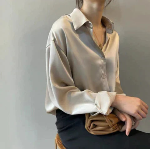 Elegant women's satin button-up shirt featuring a timeless design, styled for both casual and formal occasions, paired with a sophisticated clutch for a chic look.