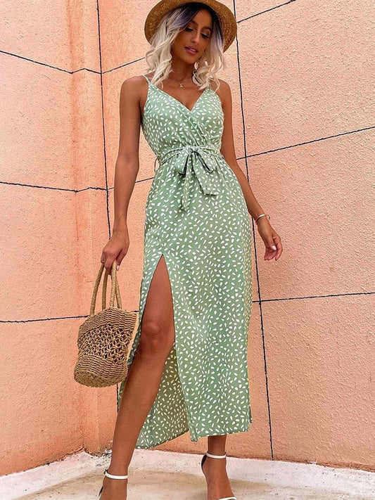 A woman wearing the Elara Women's Summer Wrap Dress with a sleeveless, wrap design, tied waist, and elegant side slits. This stylish and lightweight dress is perfect for warm weather, accessorized with a woven handbag and strappy heels for a chic summer look.