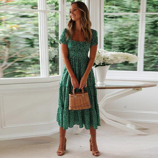 Woman wearing the Lily Women's Floral Midi Dress, a casual dress with a flowy, relaxed fit and delicate floral pattern, holding a woven handbag and posing elegantly indoors near a table decorated with flowers.