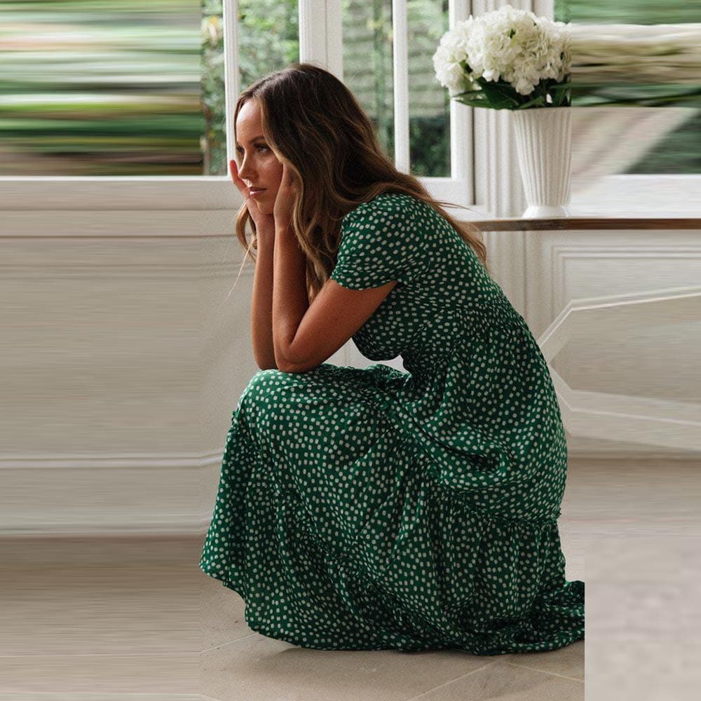 Woman wearing the Lily Women's Floral Midi Dress, a casual dress with a flowy, relaxed fit and delicate floral pattern, holding a woven handbag and posing elegantly indoors near a table decorated with flowers.