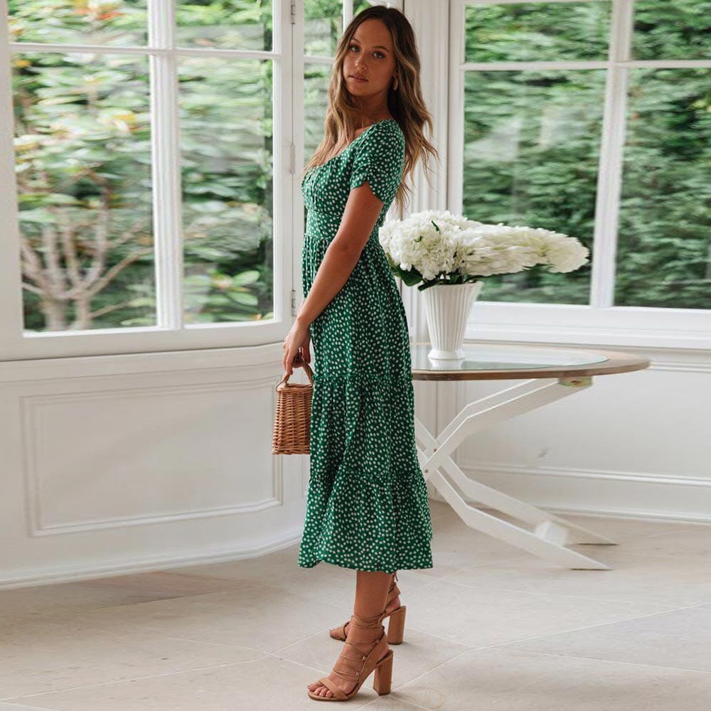 Woman wearing the Lily Women's Floral Midi Dress, a casual dress with a flowy, relaxed fit and delicate floral pattern, holding a woven handbag and posing elegantly indoors near a table decorated with flowers.