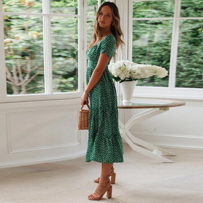 Woman wearing the Lily Women's Floral Midi Dress, a casual dress with a flowy, relaxed fit and delicate floral pattern, holding a woven handbag and posing elegantly indoors near a table decorated with flowers.