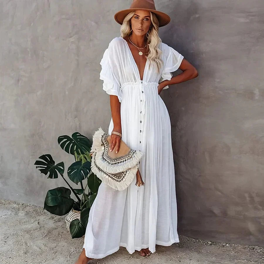 Woman wearing a wide-brimmed hat and accessorized with layered necklaces, modeling the Ivy | Flowing Bohemian Maxi Dress in an outdoor setting surrounded by natural scenery, emphasizing the dress's relaxed fit, airy fabric, and bohemian style.