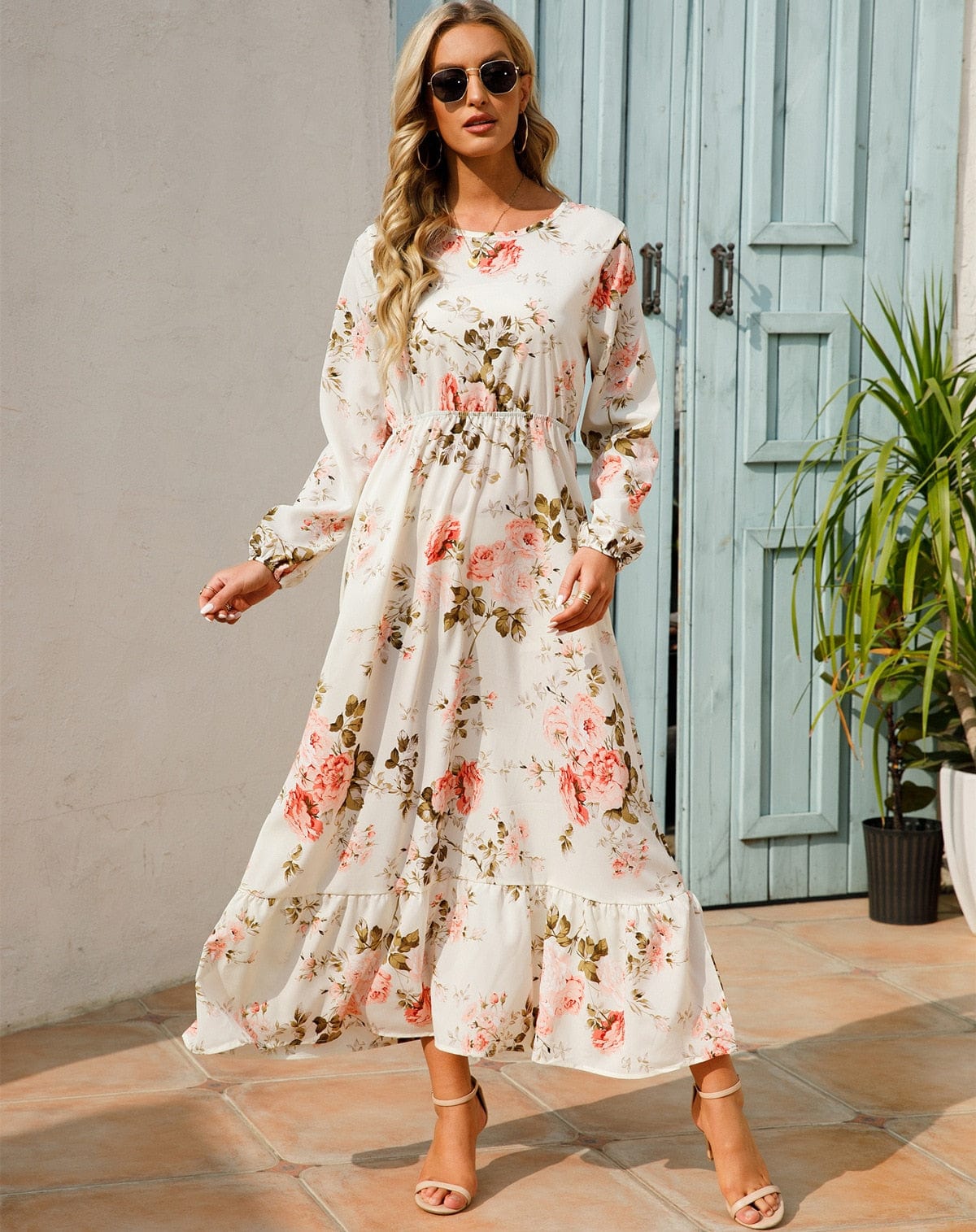 Woman wearing the Camilla Women's Floral Maxi Dress, a long dress with a flowy silhouette and elegant floral design, styled with long sleeves and paired with strappy heels, standing outdoors in a sunny, stylish setting.
